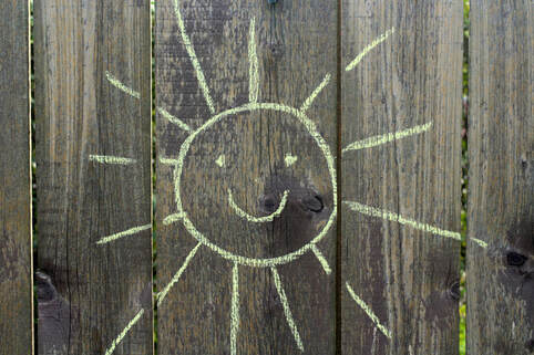 Photo of a wood fence with a chalk drawing of a smiling sun