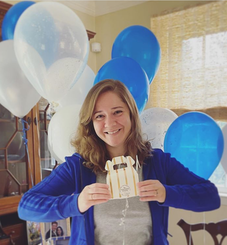 Woman holding small gift box with blue and white balloons in the background